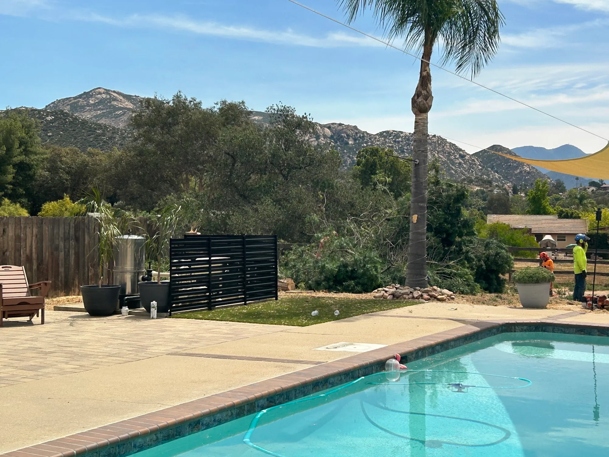 Crew clearing trees behind a pool with the Ramona hills beyond